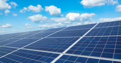 Nahaufnahme einer großen Solaranlage unter einem klaren, blauen Himmel mit vereinzelten weißen Wolken. Die Solarmodule sind gleichmäßig angeordnet und reflektieren das Sonnenlicht.