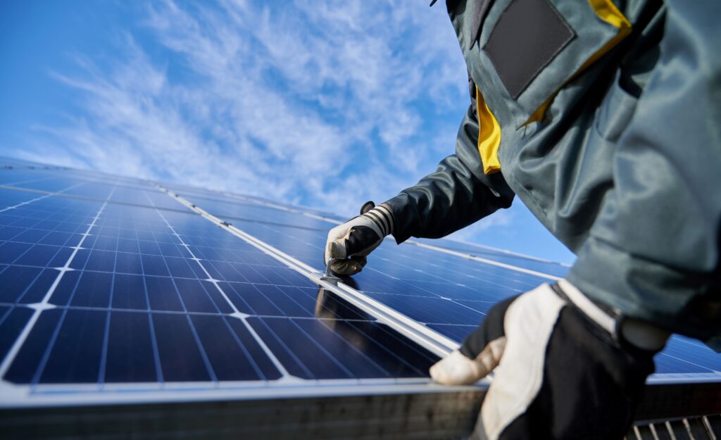 Nahaufnahme eines Technikers in Arbeitshandschuhen, der unter einem wunderschönen blauen Himmel mit Wolken eine eigenständige Photovoltaik-Solaranlage installiert. Konzept alternativer Energie und nachhaltiger Energieressourcen