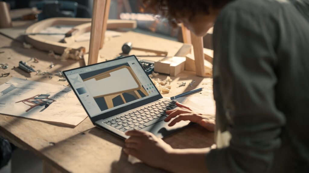 Nahaufnahme eines Möbeldesigners, der an einem Laptop arbeitet und ein digitales 3D-Modell eines stilvollen Nachttischs aus Holz erstellt. Kreative Person, die einen Entwurf für ein Tischlereiprojekt auf einem Bildschirm vorbereitet. 