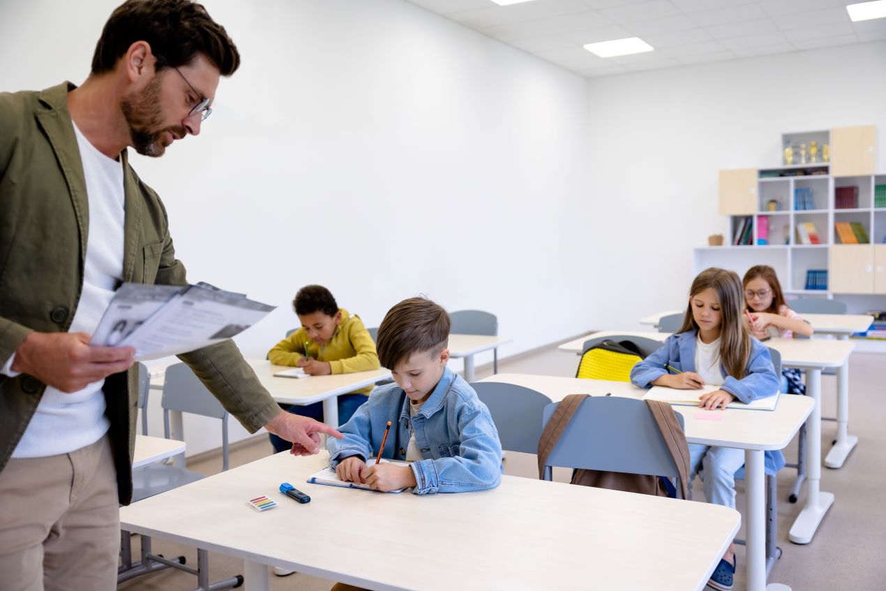 Ein Lehrer erklärt Grundschülern eine Aufgabe im Klassenzimmer – Informationen zu den Kosten einer Privatschule in Berlin