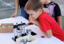 Junge bedient eine manuelle Buttonmaschine an einem Tisch mit Button-Rohlingen