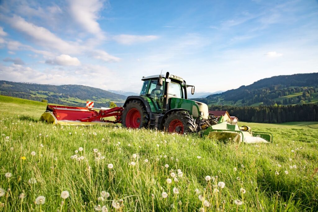 Traktor mit Anbaugeraet auf weiter Bergwiese – idealer Einsatzort fuer einen Flaechenhaecksler kaufen-Vergleich