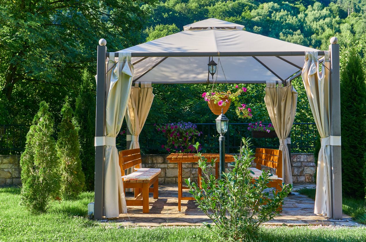 Gartenpavillons modern und funktional – ueberdachte Sitzgruppe mit Vorhaengen im gruenden Garten